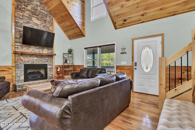 living room with wood ceiling, light hardwood / wood-style flooring, a stone fireplace, and wooden walls