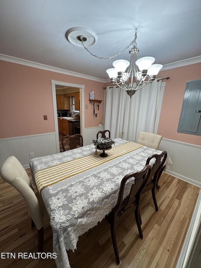 dining area with wood-type flooring, ornamental molding, electric panel, and an inviting chandelier