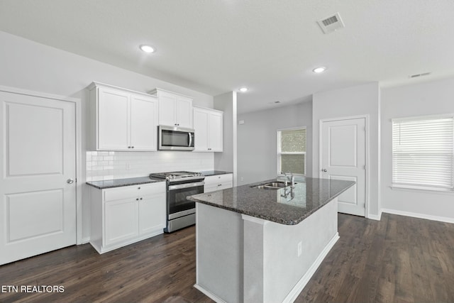 kitchen featuring sink, appliances with stainless steel finishes, white cabinetry, a kitchen island with sink, and dark stone counters