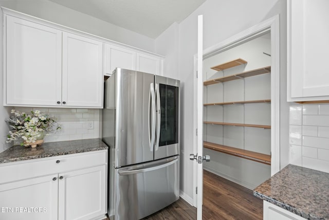 kitchen with white cabinetry, tasteful backsplash, stainless steel refrigerator, and dark stone countertops