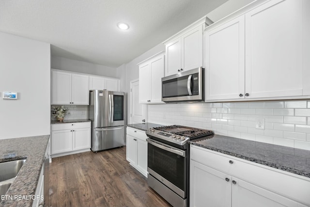 kitchen with stainless steel appliances, dark stone counters, and white cabinets