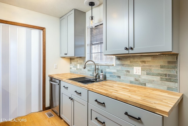 kitchen featuring butcher block counters, sink, hanging light fixtures, dishwasher, and gray cabinets