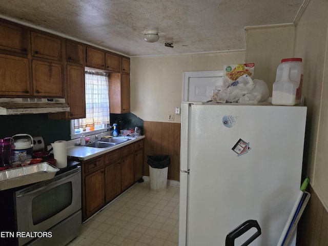 kitchen featuring sink, white fridge, a textured ceiling, stainless steel electric range oven, and wood walls