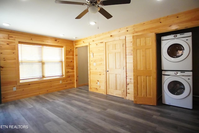 washroom featuring stacked washer and dryer, dark wood-type flooring, ceiling fan, and wood walls