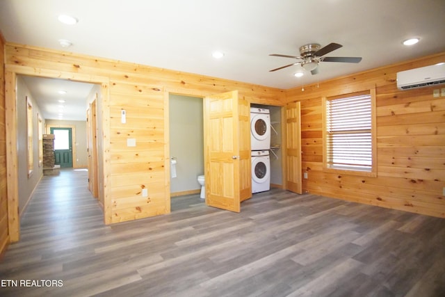 unfurnished bedroom featuring wood-type flooring, stacked washer / drying machine, a wall mounted AC, and wooden walls