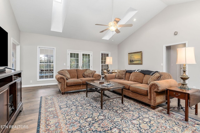 living room with high vaulted ceiling, a skylight, ceiling fan, dark wood-type flooring, and french doors