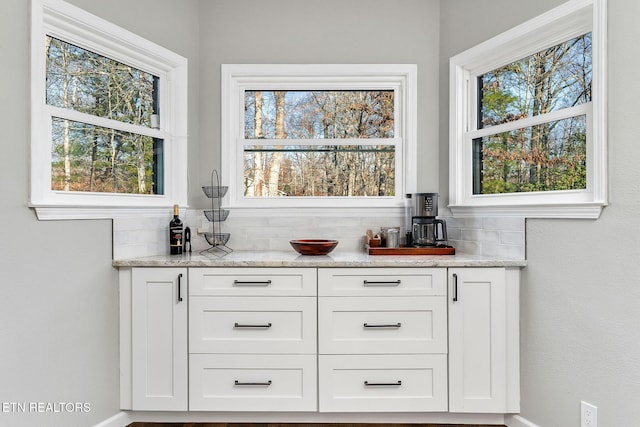 bar with tasteful backsplash, white cabinets, and light stone counters