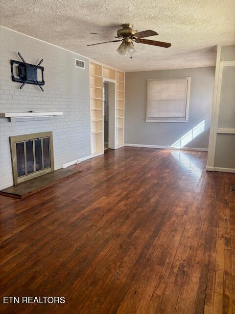 unfurnished living room with wood-type flooring, a brick fireplace, ceiling fan, and a textured ceiling