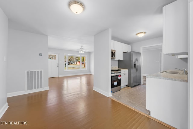 kitchen with sink, appliances with stainless steel finishes, ceiling fan, light hardwood / wood-style floors, and white cabinets