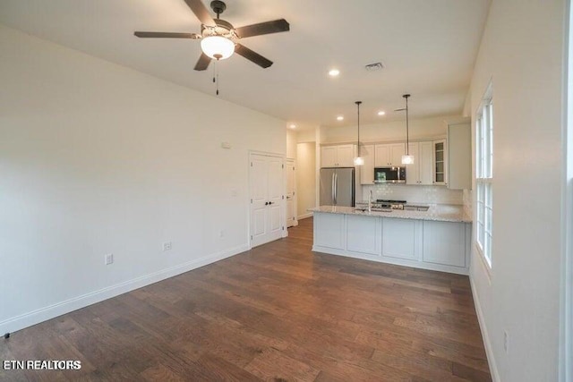 kitchen with dark wood-type flooring, appliances with stainless steel finishes, hanging light fixtures, light stone countertops, and white cabinets