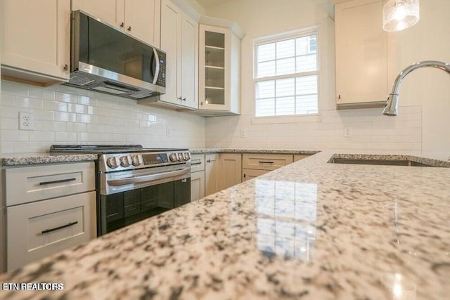 kitchen featuring appliances with stainless steel finishes, white cabinetry, sink, backsplash, and light stone countertops