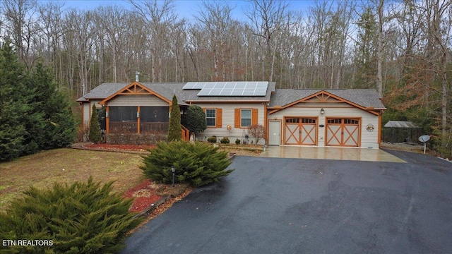 view of front of home featuring a garage, a sunroom, a front yard, and solar panels