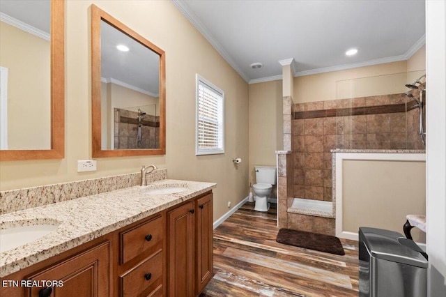 bathroom featuring hardwood / wood-style flooring, ornamental molding, vanity, tiled shower, and toilet