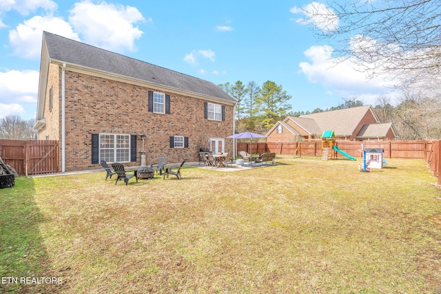 back of house featuring a playground, an outdoor fire pit, a yard, a fenced backyard, and a patio area