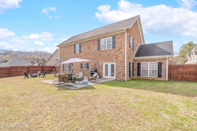 rear view of property featuring brick siding, roof with shingles, a lawn, a fenced backyard, and a patio area