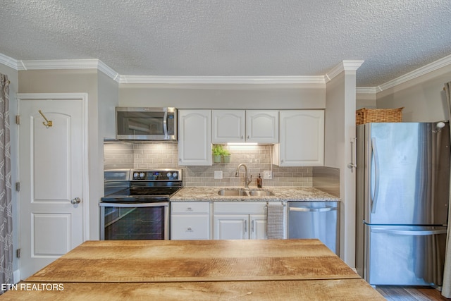 kitchen with sink, tasteful backsplash, ornamental molding, appliances with stainless steel finishes, and white cabinets