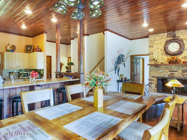 dining room featuring ornamental molding, a stone fireplace, wood-type flooring, and wood ceiling