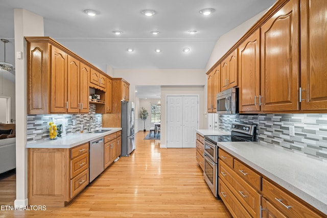 kitchen featuring sink, vaulted ceiling, light wood-type flooring, appliances with stainless steel finishes, and decorative backsplash