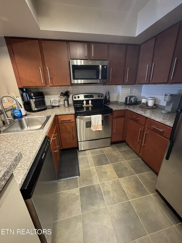 kitchen featuring appliances with stainless steel finishes, sink, dark tile patterned flooring, backsplash, and light stone countertops