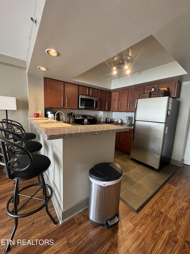 kitchen featuring dark wood-type flooring, a breakfast bar area, appliances with stainless steel finishes, kitchen peninsula, and a raised ceiling