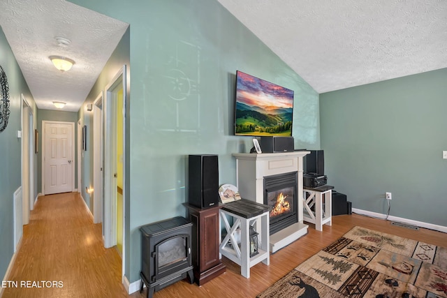 living area with a glass covered fireplace, a wood stove, wood finished floors, and visible vents