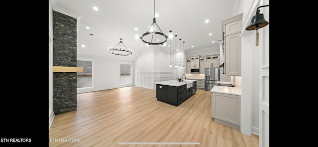 kitchen featuring appliances with stainless steel finishes, decorative light fixtures, an island with sink, ornamental molding, and light hardwood / wood-style flooring