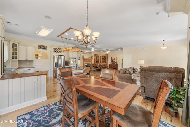 dining area featuring ornamental molding, sink, ceiling fan with notable chandelier, and light hardwood / wood-style floors