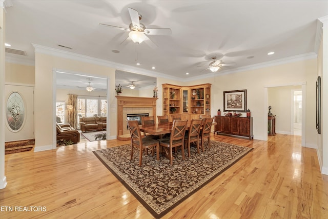 dining room featuring ceiling fan, ornamental molding, light hardwood / wood-style floors, and a tile fireplace