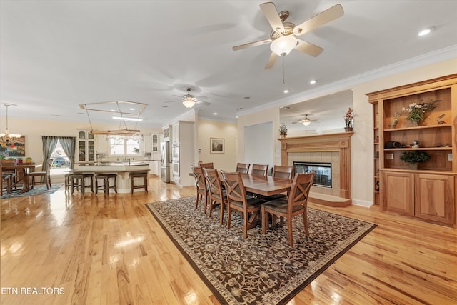 dining area featuring light hardwood / wood-style flooring, ornamental molding, a tile fireplace, and ceiling fan