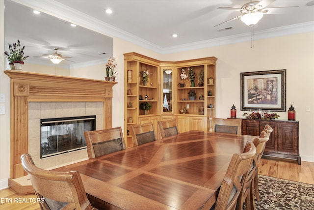 dining area with hardwood / wood-style flooring, ornamental molding, ceiling fan, and a tile fireplace