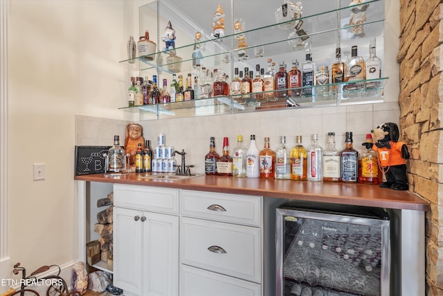 bar with butcher block countertops, sink, white cabinets, beverage cooler, and decorative backsplash