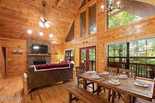 dining room featuring wooden walls, a stone fireplace, high vaulted ceiling, and light wood-type flooring