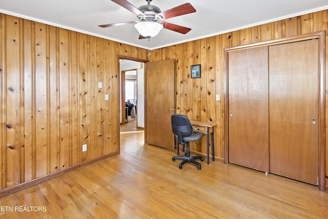 unfurnished office featuring ceiling fan, wood walls, ornamental molding, and light wood-type flooring