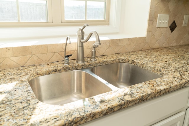 room details with white cabinetry, sink, and light stone counters