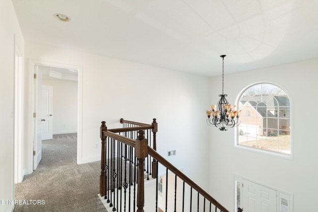 corridor with an inviting chandelier and light colored carpet