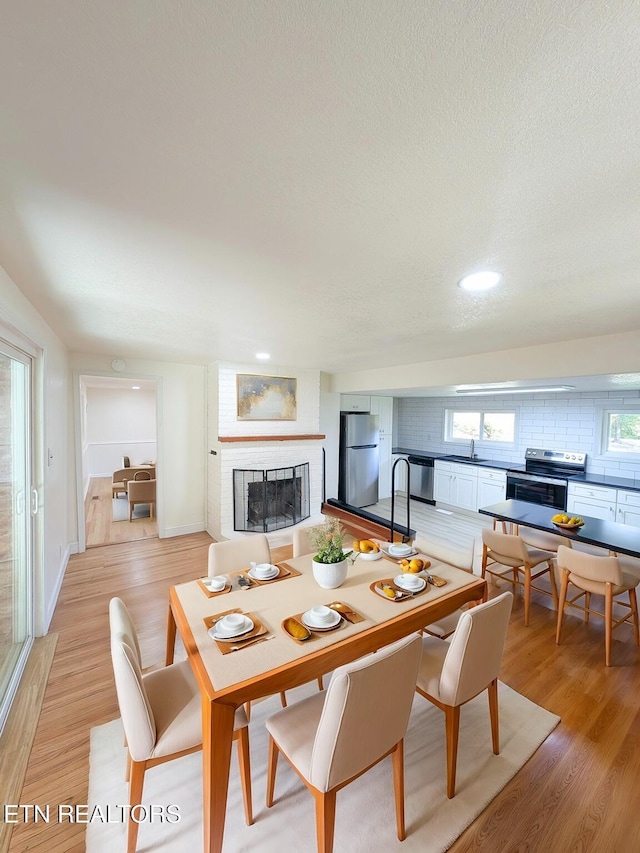 dining room featuring sink, light hardwood / wood-style floors, a brick fireplace, and a textured ceiling