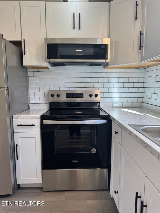 kitchen with white cabinetry, appliances with stainless steel finishes, light stone counters, and backsplash