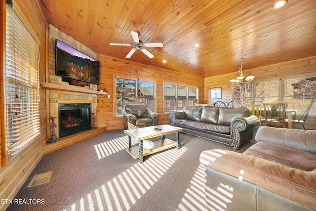 carpeted living room featuring ceiling fan with notable chandelier, wooden ceiling, a fireplace, and wood walls