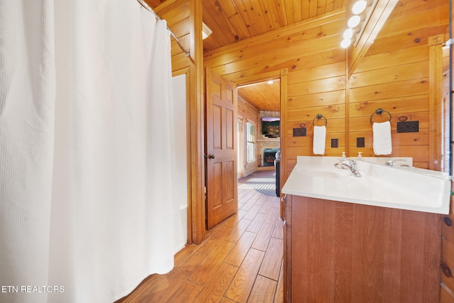 bathroom featuring wood walls, wooden ceiling, vanity, beamed ceiling, and a fireplace