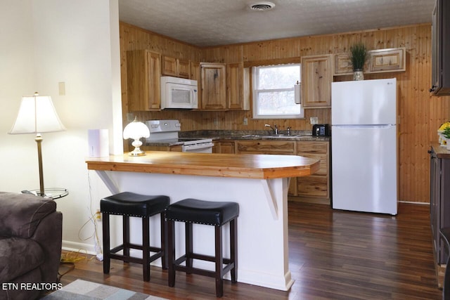 kitchen featuring sink, white appliances, wooden walls, a kitchen breakfast bar, and kitchen peninsula