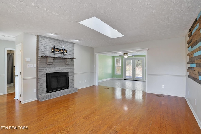 unfurnished living room featuring french doors, wood-type flooring, a brick fireplace, and a textured ceiling