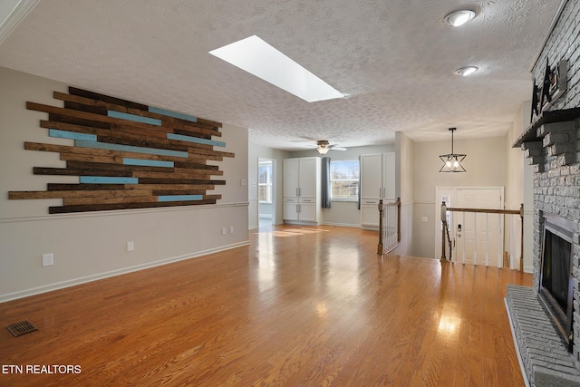 unfurnished living room featuring a brick fireplace, a textured ceiling, light wood-type flooring, and a skylight