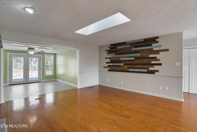 unfurnished room featuring ceiling fan, hardwood / wood-style floors, a skylight, a textured ceiling, and french doors