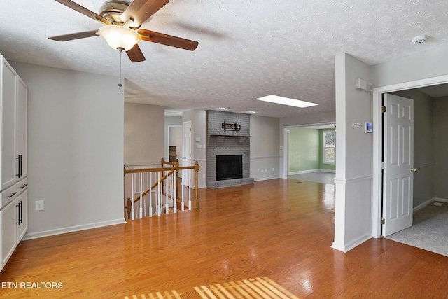 unfurnished living room featuring hardwood / wood-style flooring, ceiling fan, a brick fireplace, and a textured ceiling