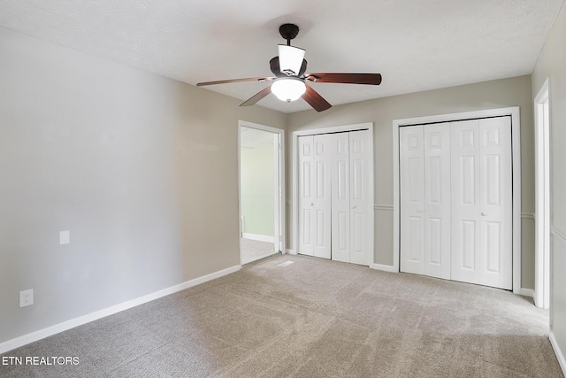 unfurnished bedroom with light carpet, two closets, and ceiling fan