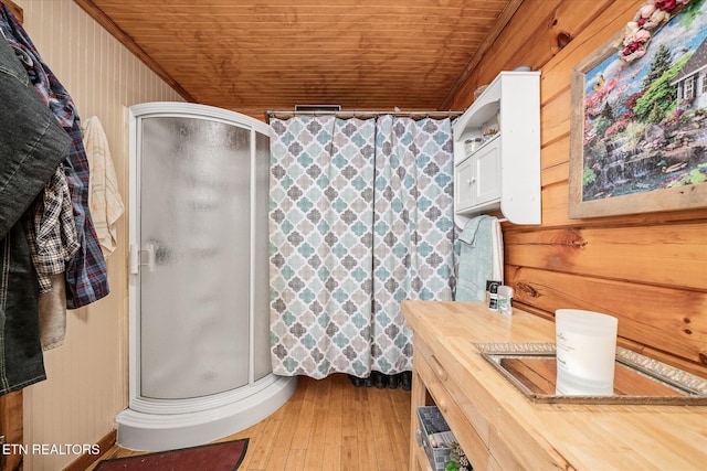 bathroom featuring hardwood / wood-style floors, wooden walls, vanity, a shower with door, and wooden ceiling