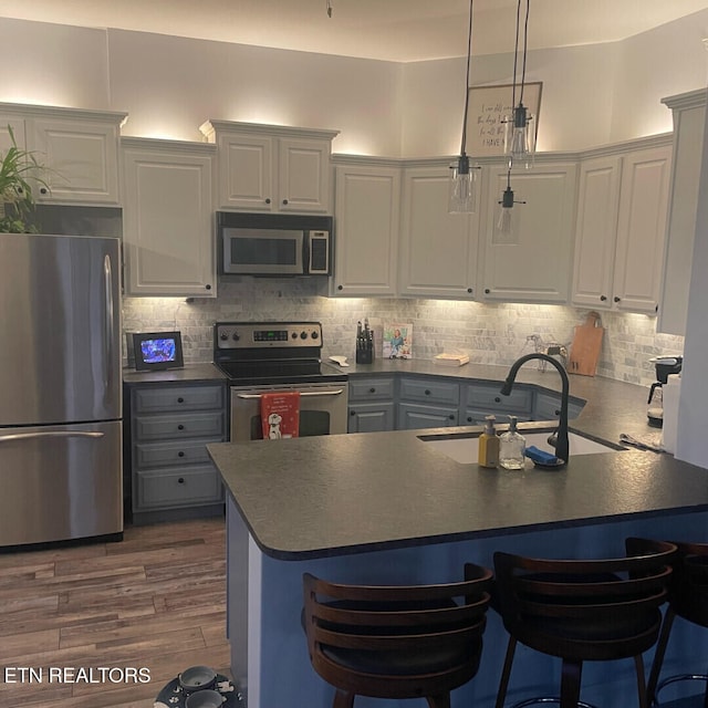 kitchen with sink, white cabinetry, kitchen peninsula, pendant lighting, and stainless steel appliances