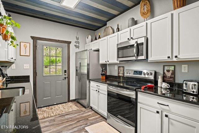 kitchen with sink, white cabinetry, light hardwood / wood-style flooring, dark stone countertops, and stainless steel appliances