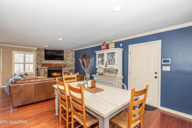 dining room with crown molding, hardwood / wood-style flooring, and a stone fireplace