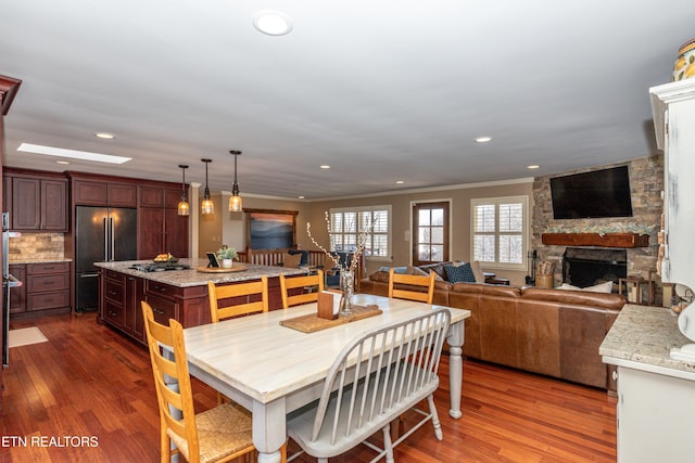 dining room with a stone fireplace, a skylight, ornamental molding, and dark hardwood / wood-style floors